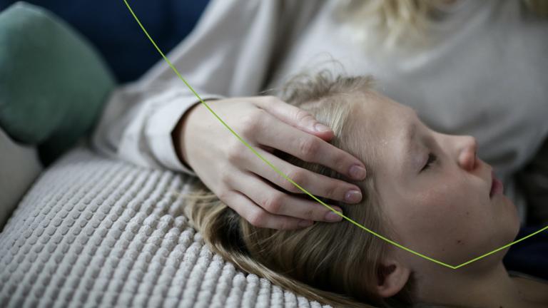 kind ligt met hoofd op kussen en heft hand op het hoofd van ouder