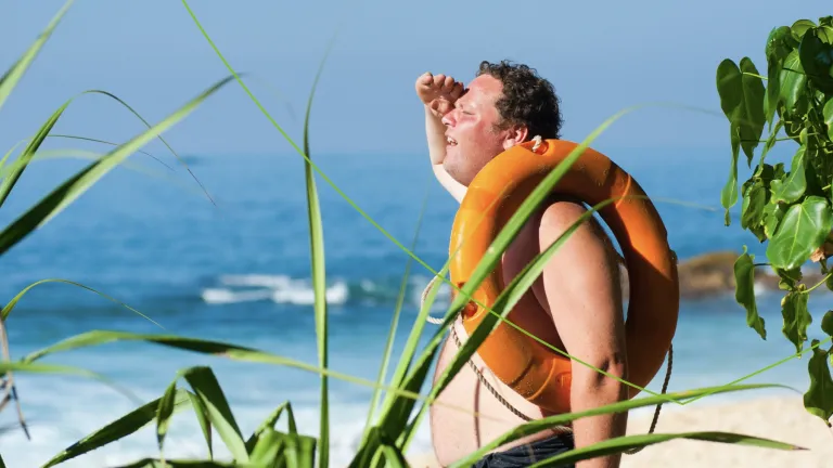 Man met reddingsband op het strand die in de verte kijkt