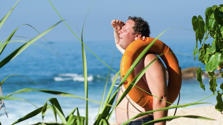 Man met reddingsband op het strand die in de verte kijkt