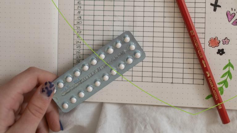 strip met anticonceptiepil wordt vastgehouden met op de achtergrond een blaadje met ta en een potlood