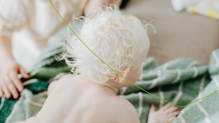 baby met blond haar met blote rug kruipt op de grond op een kleed