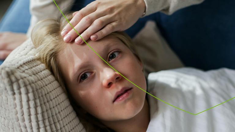 Kind ligt ziek op bank, ouder houdt hand op het hoofd